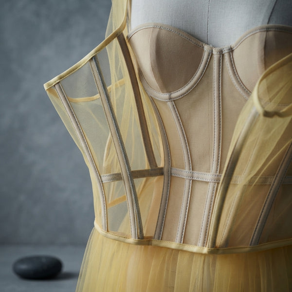 Close-up of the internal boning and structured bodice construction of a yellow tulle gown on a neutral gray background.