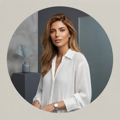 Portrait of influencer Negin Mirsalehi wearing a white long-sleeved pleated shirt against a minimalist gray background.