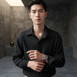 A model wearing a white long-sleeved pleated dress shirt in a professional portrait against a minimalist charcoal backdrop.