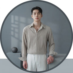 A professional portrait of a man wearing a white long-sleeved pleated dress shirt against a minimalist neutral background.