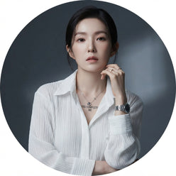 A professional circular portrait of Irene Kim wearing a white pleated long-sleeved shirt against a minimalist gray background
