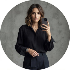 Jeanne Damas posing in a pleated white long-sleeved shirt against a neutral slate gray studio background.